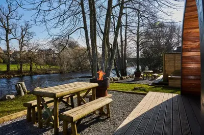 a picnic table with a fire next to a river at Braidhaugh Holiday Lodge and Glamping Park in Crieff