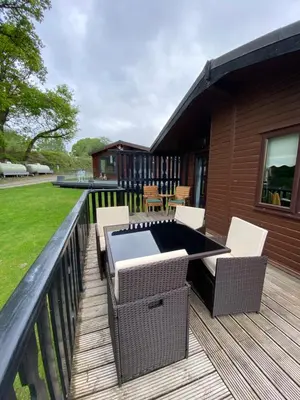 a deck with chairs and a grill on a house at Cozy Loch Lomond Lodge 27, Rowardennan in Rowardennan