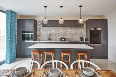 a kitchen with gray cabinets and a counter with stools at Beach House in Pennygown