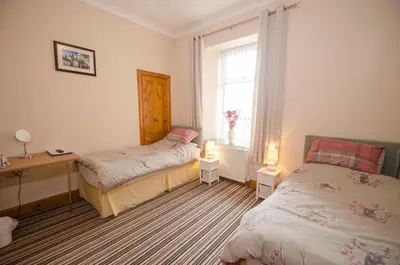 a bedroom with two beds and a desk and a window at Knight's Rest Guest House in Airdrie