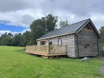 a large wooden cabin with a deck in a field at Loch Aweside Forest Cabins in Dalavich