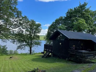 a black cabin on the side of a lake at Loch Aweside Forest Cabins in Dalavich
