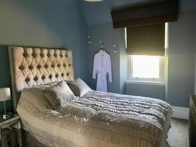 a bedroom with a bed and a dress hanging in a window at Pollokshields Burgh Hall Lodge Houses in Glasgow