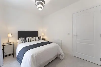 a white bedroom with a bed with a black headboard at Mhuilinn Apartment in Stirling