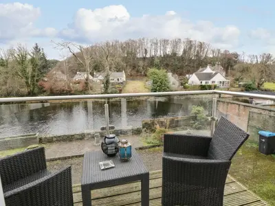 a table and two chairs on a deck with a view of a river at Barley Cottage in Newton Stewart