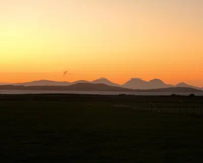 a sunset over a field with mountains in the background at Primrose Cottage in Killean