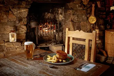 a table with a plate of food and a glass of beer at Oak Tree Inn in Balmaha