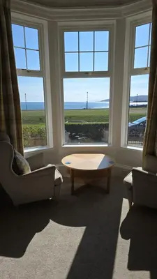 a living room with two chairs and a table and windows at 4 Kames Bay in Millport
