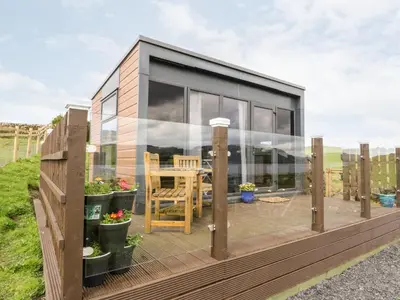 a small house with glass walls and a wooden deck at Balvicar Beag in Oban