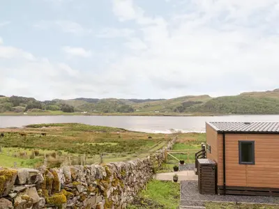 a cabin with a stone wall next to a lake at Balvicar Beag in Oban