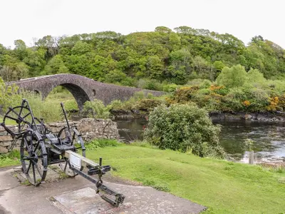 a bench sitting next to a river with a bridge at Balvicar Beag in Oban