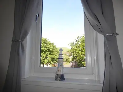 a window with a lighthouse sitting on a window sill at Cove Bay 1 Bed Flat in Largs