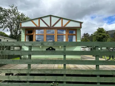 a green house with a large window behind a fence at The Lambourne 71 in Dunoon