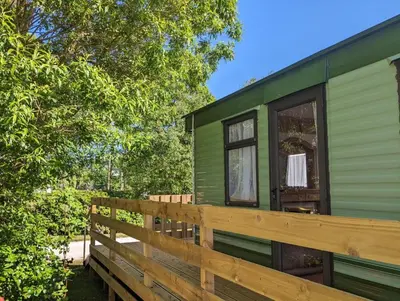 a green tiny house with a wooden deck at 55 Glenfinart Caravan Park in Dunoon
