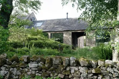 an old stone house behind a stone wall at Eastside - Architect designed retreat with wood-fired sauna in Penicuik