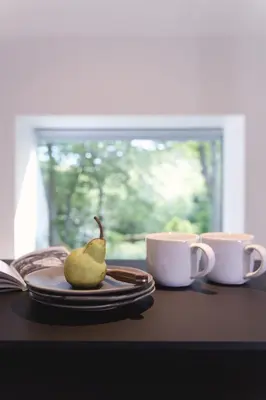 a plate with a pear on a table next to two cups at Eastside - Architect designed retreat with wood-fired sauna in Penicuik