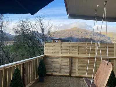 a porch with a swing on a deck with mountains at Devon River Glamping Pods in Alloa