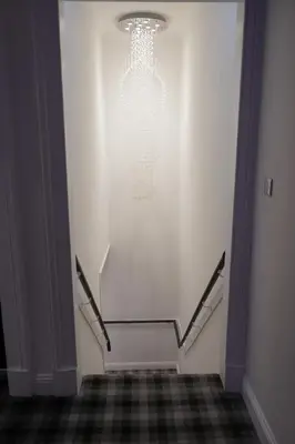 a hallway with a white wall with a chandelier at Novana Aparthotel in Glasgow