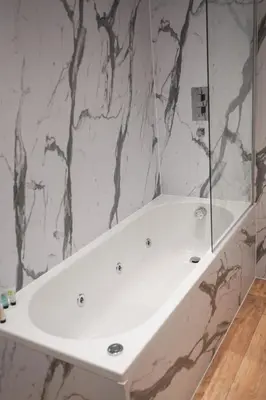 a white tub in a bathroom with a marble wall at Novana Aparthotel in Glasgow