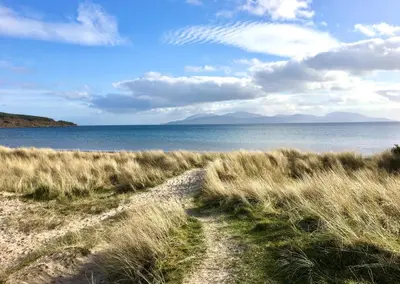 a path through a field of grass next to the water at Burnside in Tighnabruaich