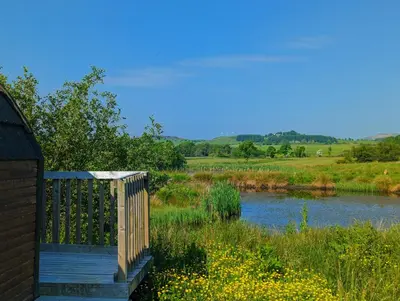 a wooden bridge over a river next to a field at Pond View Pod 2 with Private Hot Tub - Fife - Loch Leven - Lomond Hills in Kelty