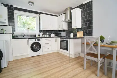 a kitchen with white cabinets and a washer and dryer at Rotherwood Apartment in Glasgow