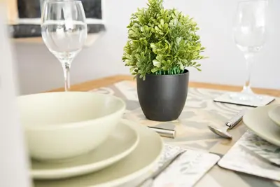 a table with plates and glasses and a plant at Rotherwood Apartment in Glasgow