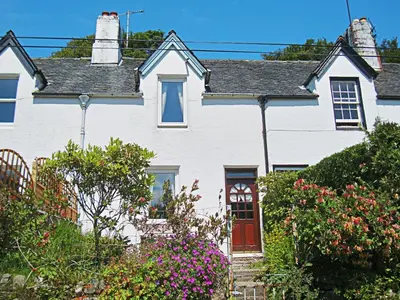 a white house with a red door and some flowers at 15 Cairnbaan Cottage in Cairnbaan