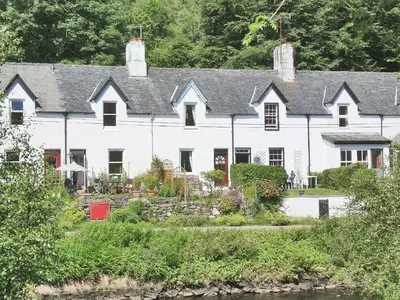 a white house with a river in front of it at 15 Cairnbaan Cottage in Cairnbaan