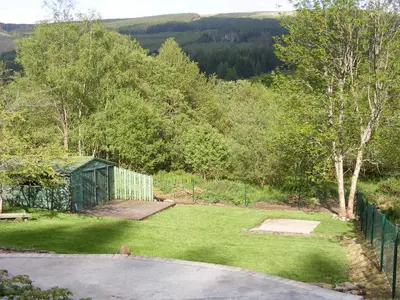 a garden with a fence and a green building at Tigh Raineach in Strathyre