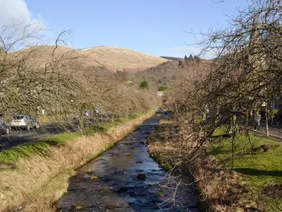 a river in a field next to a road at Inn Cottage in Glendevon