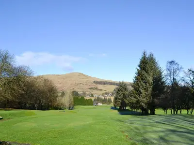 a golf course with trees and a hill in the background at Inn Cottage in Glendevon