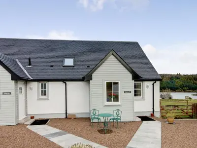 a white house with a black roof and two chairs at Kestrel Cottage - 27937 in Stirling