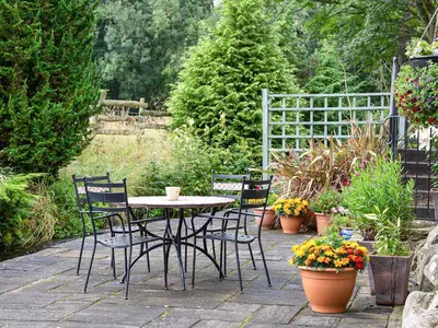 a patio with a table and chairs and plants at Fochy Cottage in Milnathort