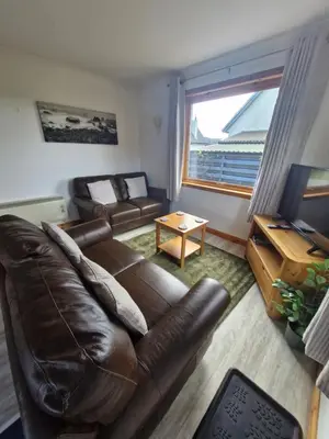 a living room with a brown leather couch and a window at Kings Reach - Dunadd Cottage in Lochgilphead
