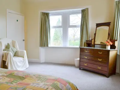 a bedroom with a dresser and a mirror and a window at Blairhosh Cottage in Balloch