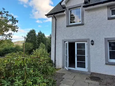 a white house with a door and a yard at Taigh Geal in Killin
