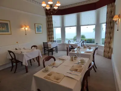 a dining room with tables and chairs and windows at Douglas Park Guest House in Dunoon