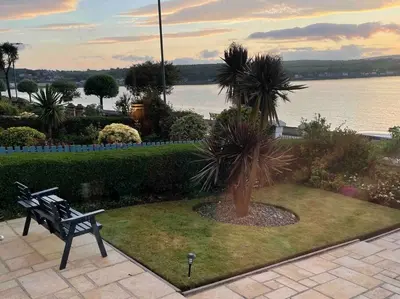 a park bench with a palm tree in front of the water at Bayside - Breathtaking views of the Clyde in Rothesay