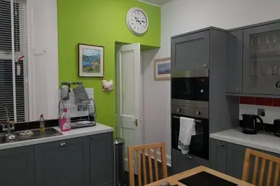 a kitchen with green walls and a clock on the wall at Snug - Fountain Bank Apartment in Helensburgh