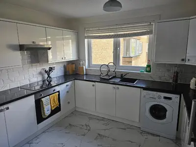 a kitchen with white cabinets and a washing machine at Snug - Colquhoun Square Apartment in Helensburgh
