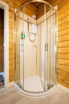 a shower with a glass enclosure in a room with wooden walls at Torr Lodge- luxury log cabin with private hot tub! in Ballycastle