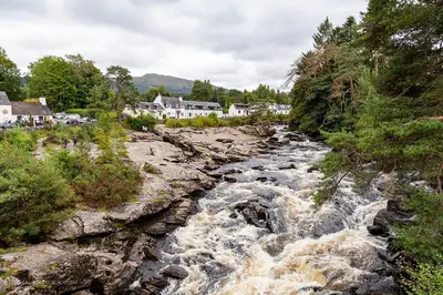 a river flowing through a town with houses at Railway Cottage in Killin