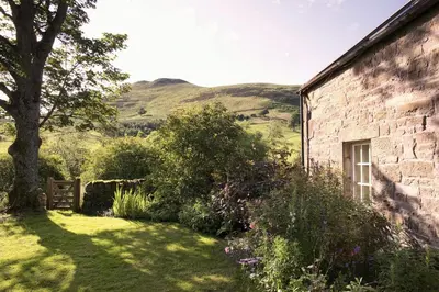 a brick building with a tree and a hill in the background at Eastside Steading - Family barn in the Pentland Hills, Edinburgh in Penicuik
