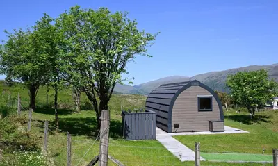 a small shed in a field with mountains in the background at Macree Pod in Taynuilt