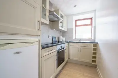 a small kitchen with white cabinets and a window at Thomas Carlyle Cottage in Thornhill