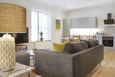 a living room with a gray couch and a kitchen at The Woodside Apartments in Doune