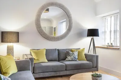 a living room with a gray couch and a mirror at The Woodside Apartments in Doune
