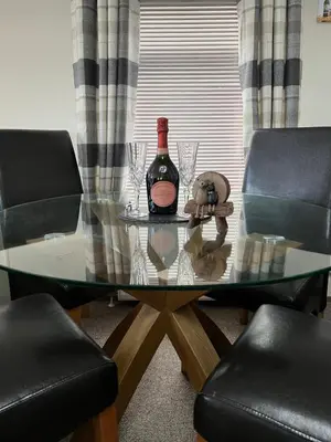 a glass table with a bottle of wine and two chairs at Maneight Luxury Lodge with hot tub in New Cumnock