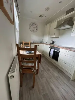 a kitchen with a table and a clock on the wall at Wee Dipper Cottage Maybole in Maybole